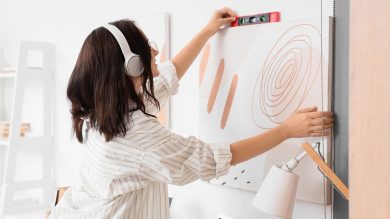 A woman in headphones hanging wall art with a level