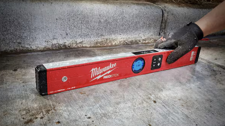 A person holding a Milwaukee Redstick Digital Box Level on a concrete surface