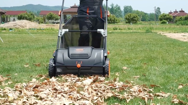 Person using VEVOR lawn sweeper to sweep up leaves on lawn