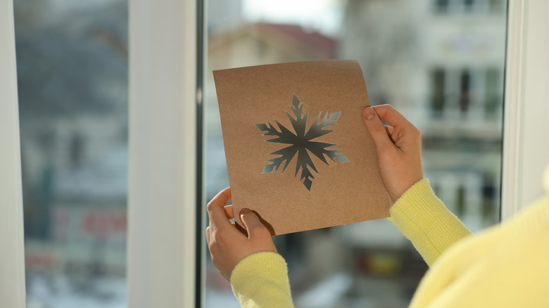 person holding snowflake stencil in front of window