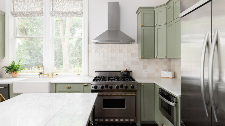 a light kitchen with sage green cabinets and gold hardware