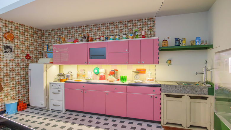 A colorful 1960s kitchen with pink cabinets and orange wall tiling.