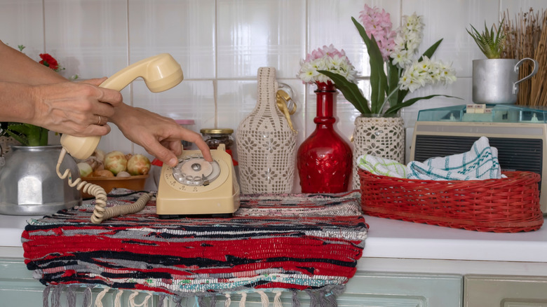 A person dialing a rotary phone in a vintage kitchen.
