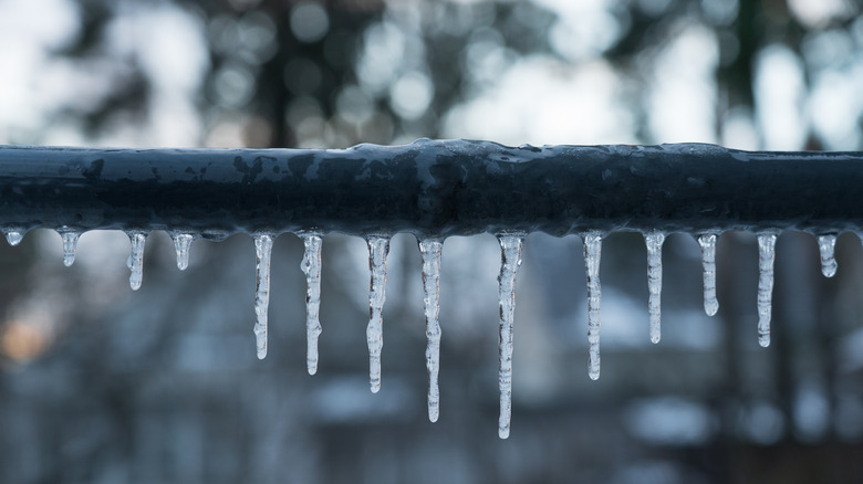 Icicles hanging on dark pipe suspended horizontally with blurred background