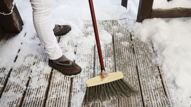 a person clearing snow from her porch and steps with a broom