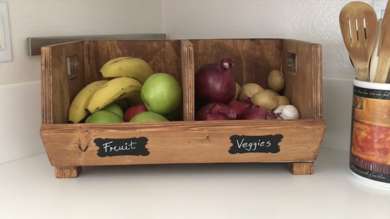 A wooden box on a countertop storing fruit on one side and vegetables on the other