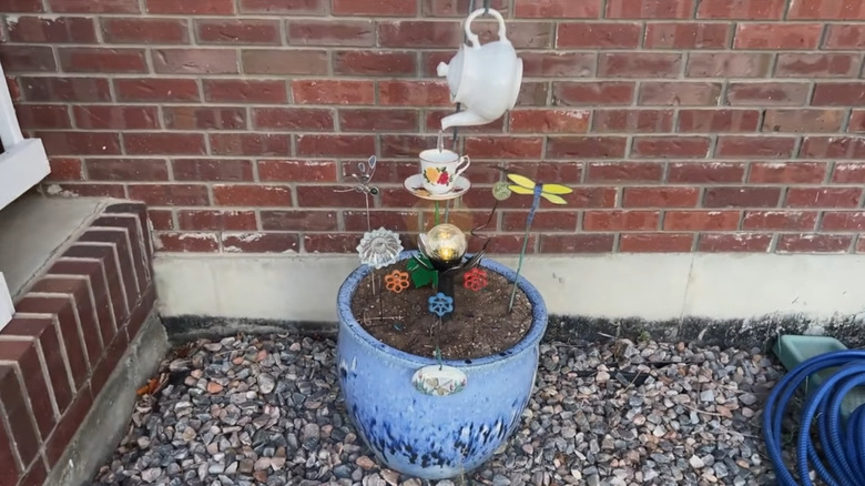 Lighted display in a planter with a teapot hanging on a hook