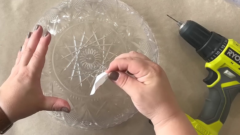 Person peeling sticker of Dollar Tree punch bowl beside an electric drill for a DIY project