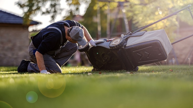 Worker inspecting underside of rotary lawn mower