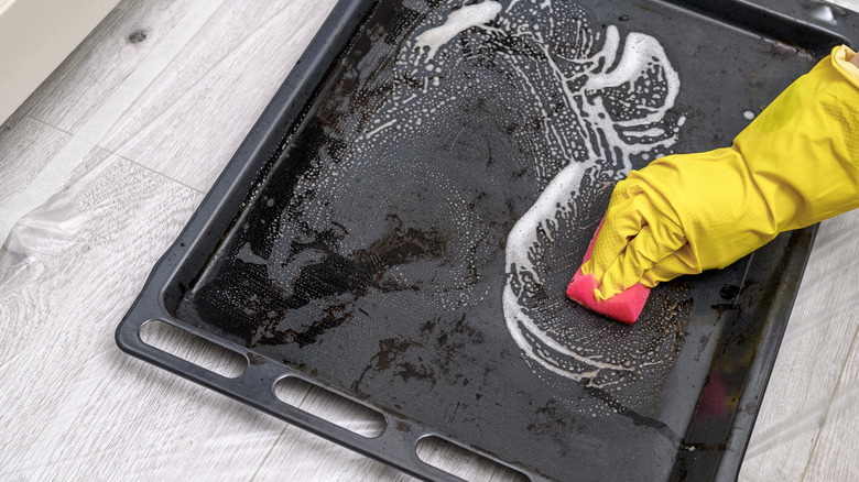 A person cleaning a baking sheet with a rubber glove