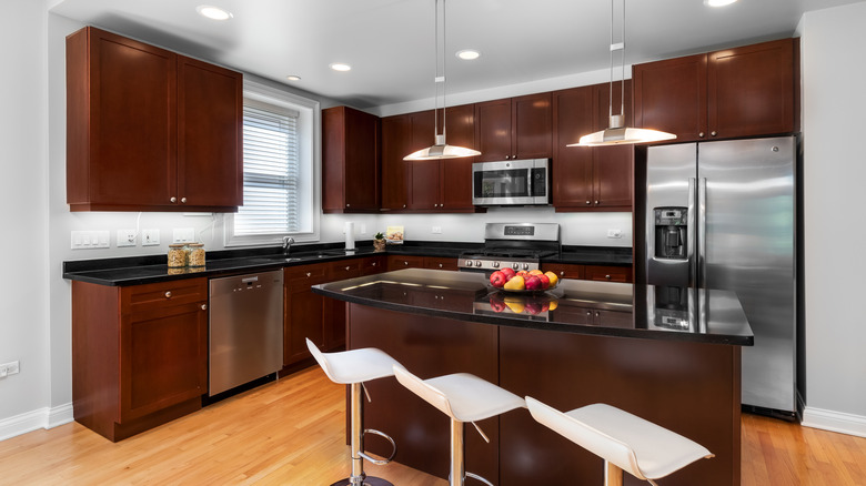 Three contemporary white bar stools sit in a kitchen with mahogany cabinets