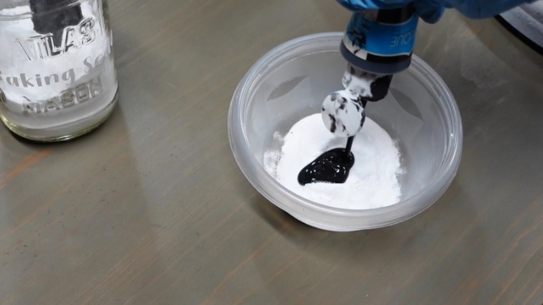 Person pouring black acrylic paint into bowl of baking soda to make textured paint