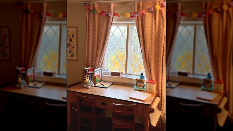 Colorful paper chain strewn across light-colored curtains above child's desk with crafts and books