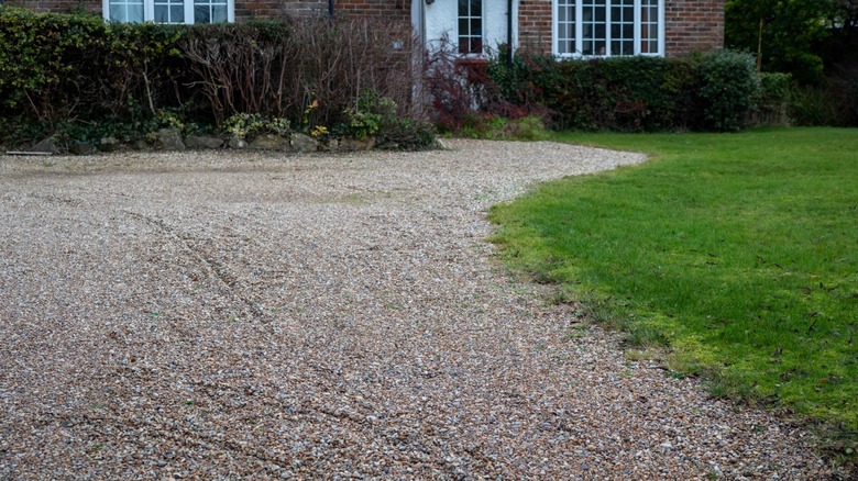 Portion of a gravel driveway with an unfinished edge. There's a house in the background