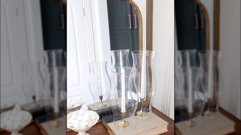 Taper candles displayed inside clear hurricane glass shades on a dresser next to a mirror