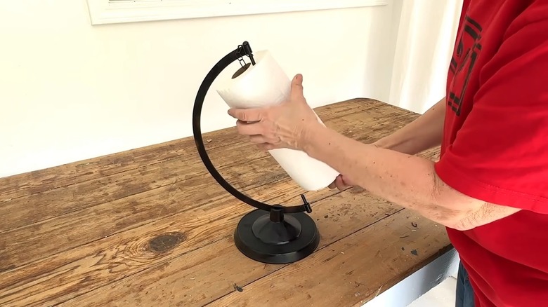 Woman looping in a paper towel roll in a metal globe stand