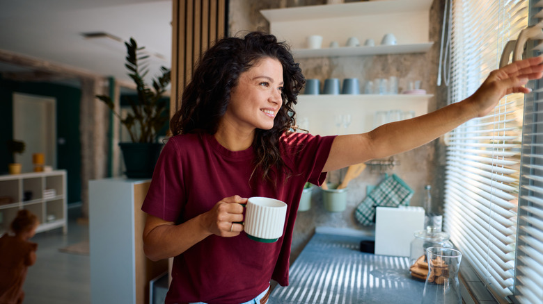 woman adjusts blinds in a kitchen window