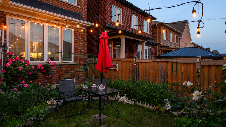 Small backyard area with dining table set, bushes, and string lights