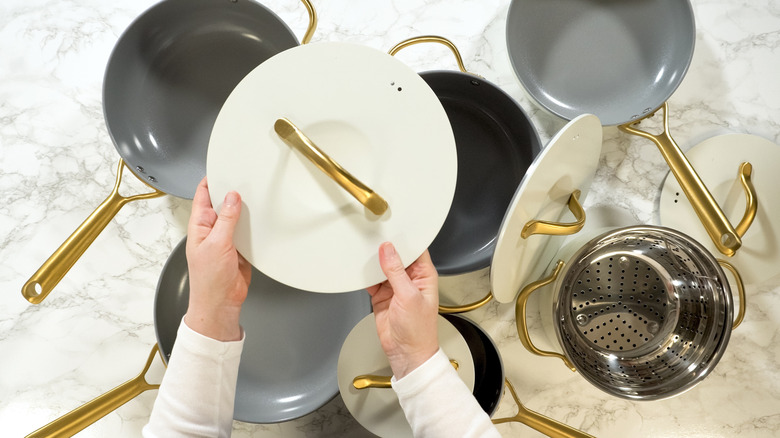 A person holding a pot lid while organizing a cookware collection