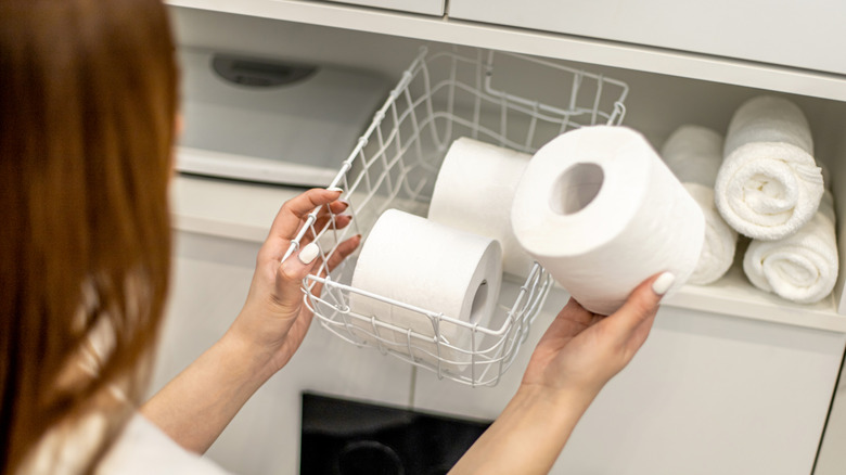 Woman trying to organize toilet paper rolls in a basket in the bathroom