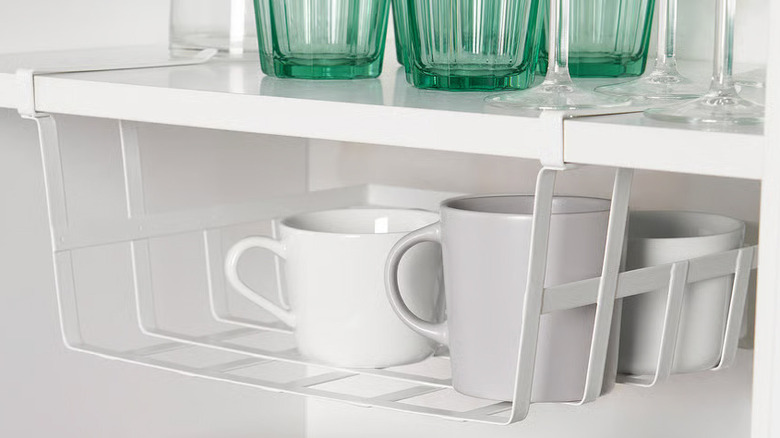 White coffee mugs sit inside a PÅLYCKE Clip-on basket under a kitchen cabinet shelf