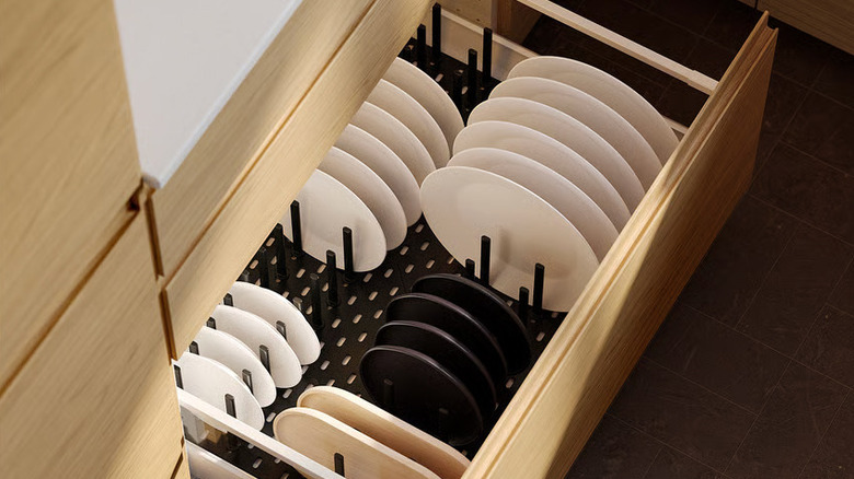 White and black plates are organized in a black pegboard inside a wooden kitchen drawer