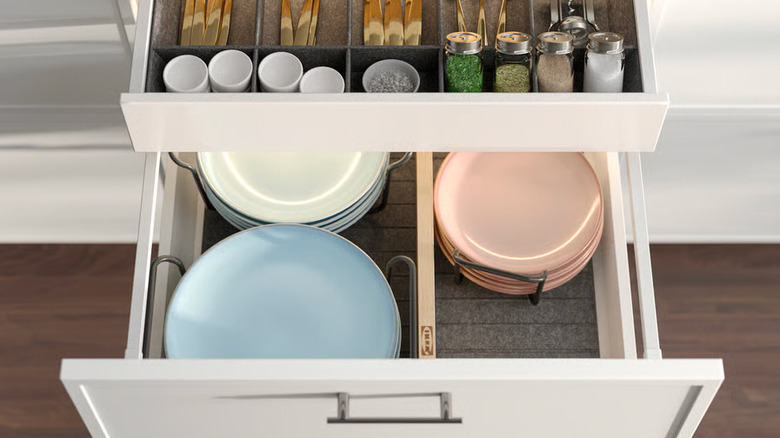 A light VARIERA Drawer divider is installed in a deep white kitchen drawer full of plates