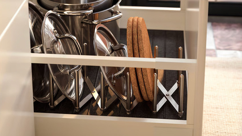Stainless steel pot lids and cork trivets rest in a VARIERA Pot Lid Organizer from IKEA
