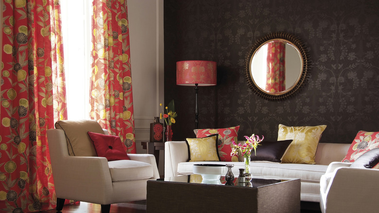 Red and gold patterned curtains part on a moody living room scene, revealing a sheer layer underneath.