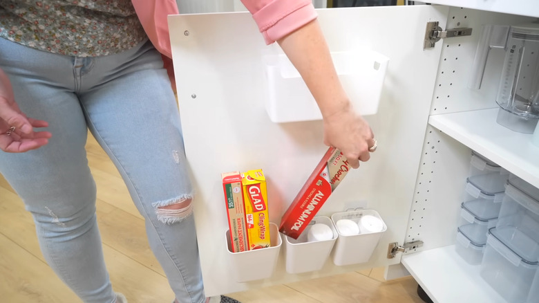Person putting aluminum foil in a plastic container on the inside of a cabinet door