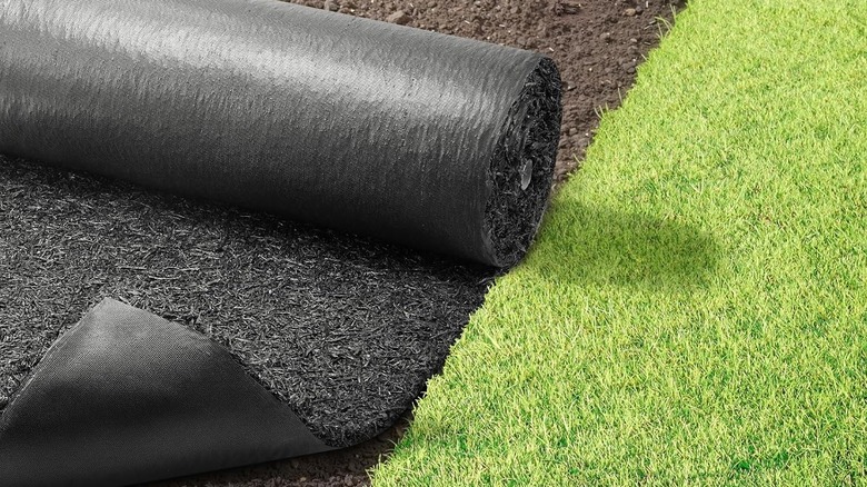 A roll of rubber mulch being unrolled in the dirt