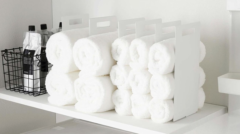 White metal dividers on a shelf with rolled up towels between them.