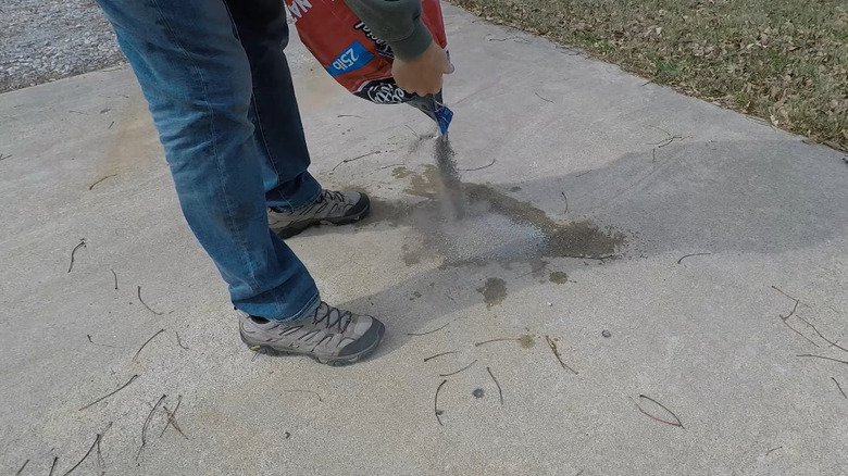 Man pouring kitty litter over an oil stain on his driveway