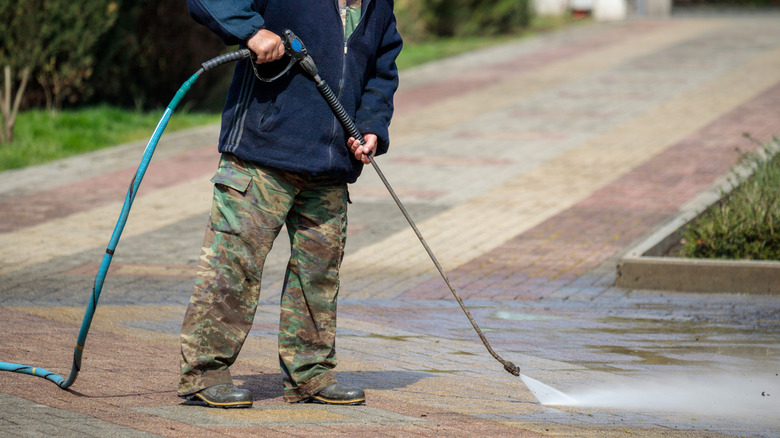 Man dressed in camo pants and thick jacket cleaning driveway with a water hose