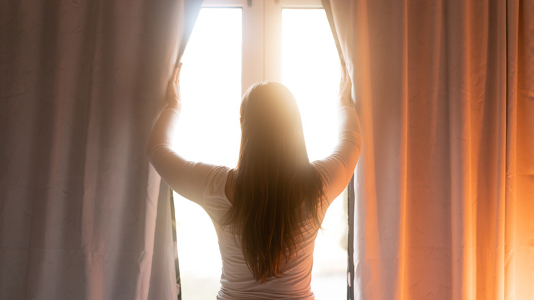 Woman between heavy curtains in bright light