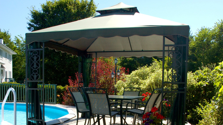 Pop-up gazebo with fabric top covering dining set by pool
