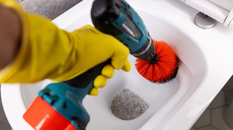 A person cleaning a toilet with a drill-powered scrub brush.