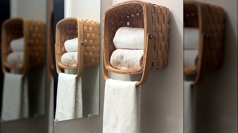Square basket mounted to the wall with rolled towels inside and a folded towel hanging on the basket handle
