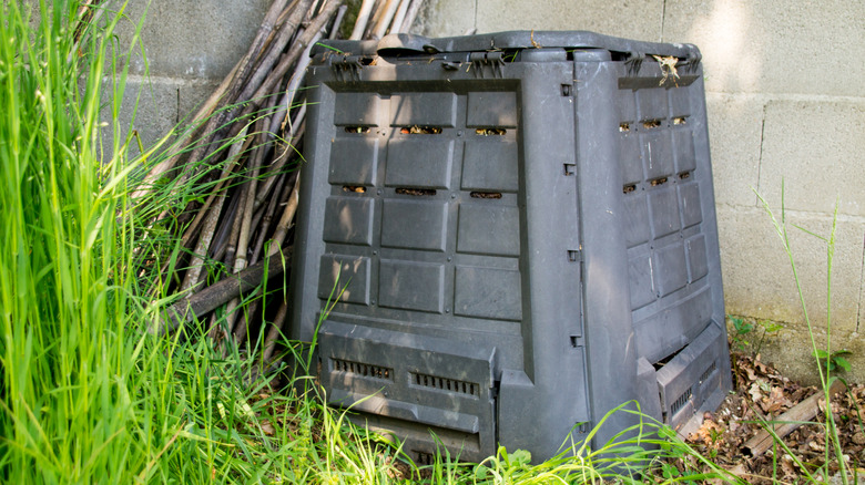 a black composter in the corner of a garden