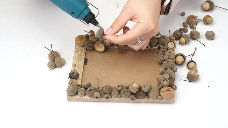 a woman glues acorns onto a picture frame