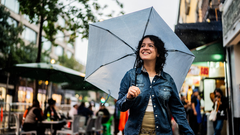 Young woman using umbrella and walking through the city