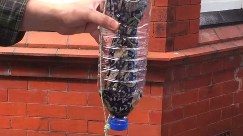 Man puts umbrella into plastic bottle umbrella storage holder in front of brick wall