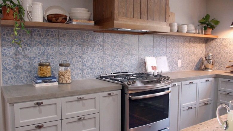 A kitchen with a cement countertop and a blue and white patterned backsplash and an open shelf.