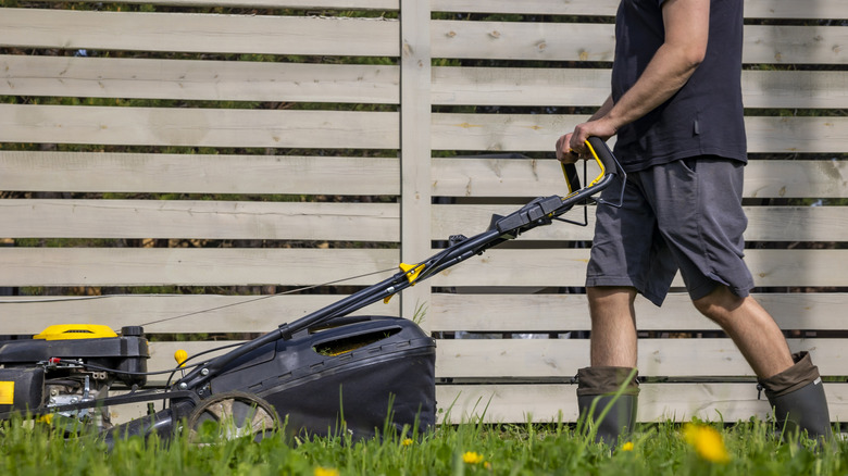 Man in boots mowing long grass with lawn mower