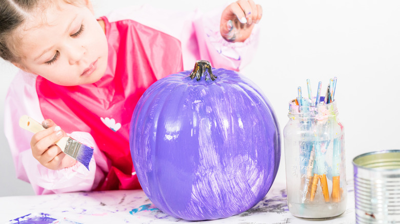 little girl painting a pumpkin purple