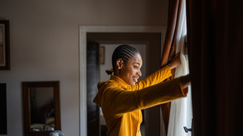 A woman opening curtains and smiling