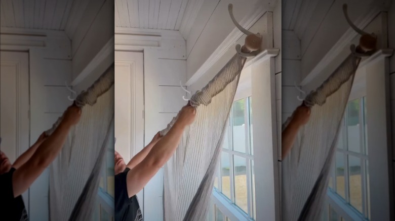 A person installs coat hook curtain rod supports in a French country-style bedroom
