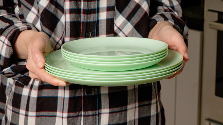 A person holding a stack of green dishes