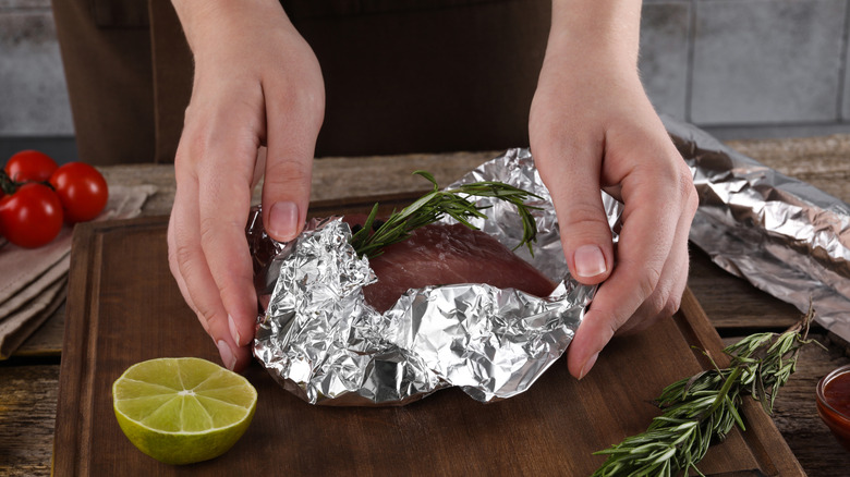 Woman's hands wrapping a piece of meat up in foil on a wooden cutting board