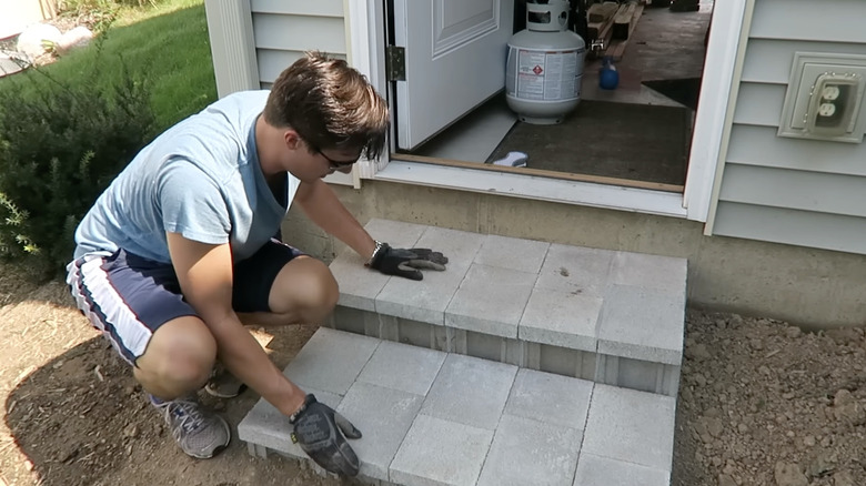 A man building small steps out of concrete blocks and pavers.